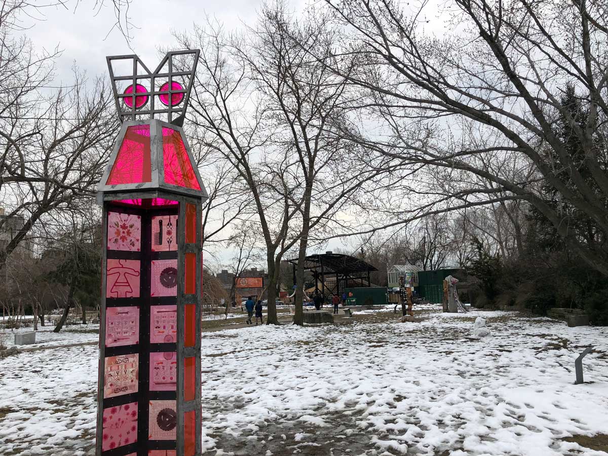 A tall pink sculpture in a park covered in snow and mud