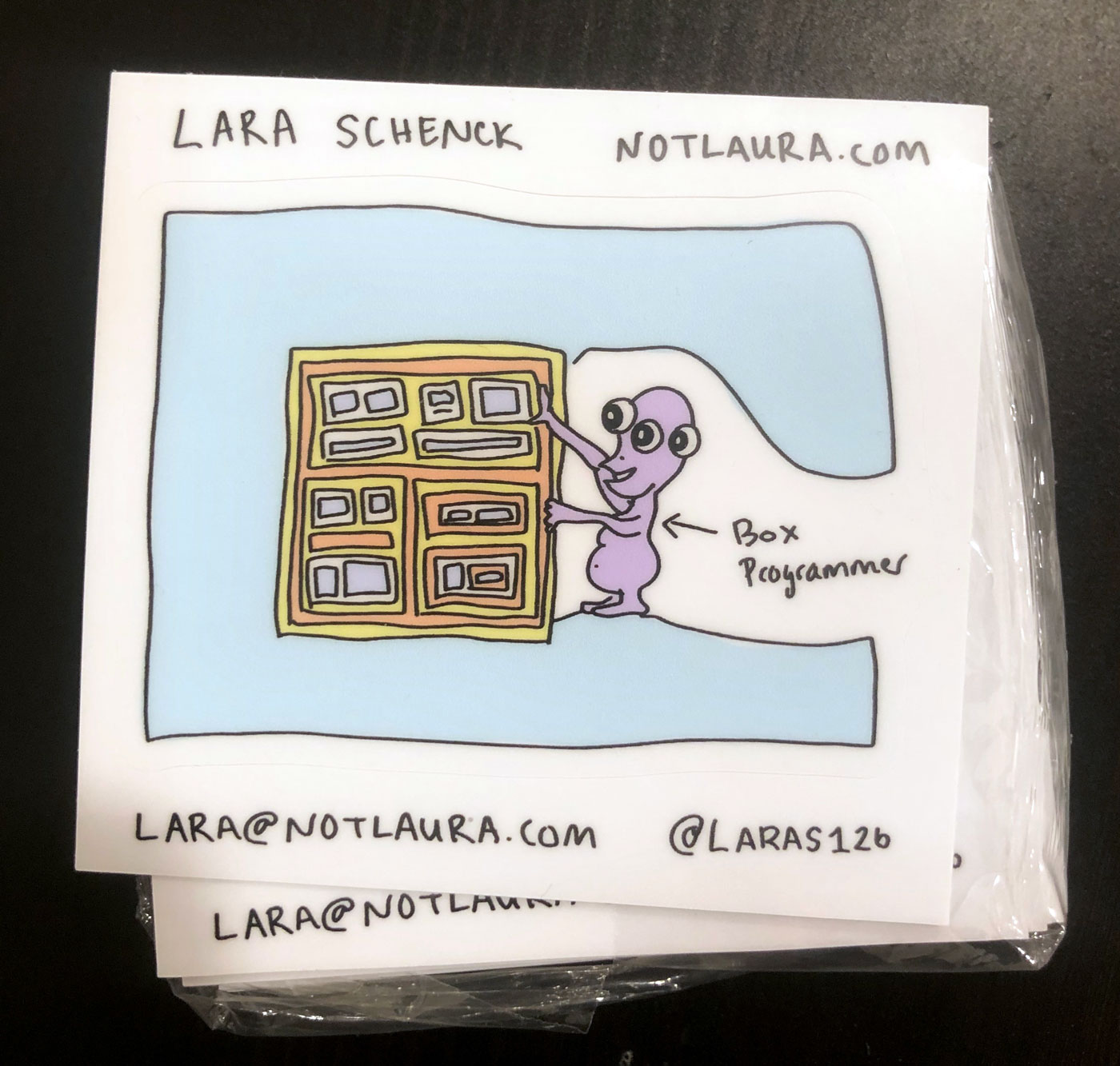 Stickers containing an illustration of a monster doing a puzzle of boxes, and an arrow pointing to the monster saying "Box Programmer" and Lara's information
